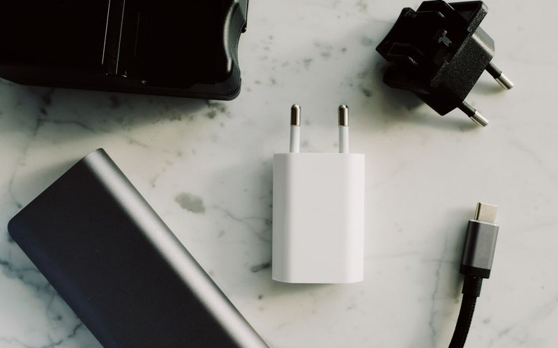 흰색 충전 어댑터, 파워뱅크, USB-C 케이블, 여행용 어댑터가 대리석 위에 놓인 모습